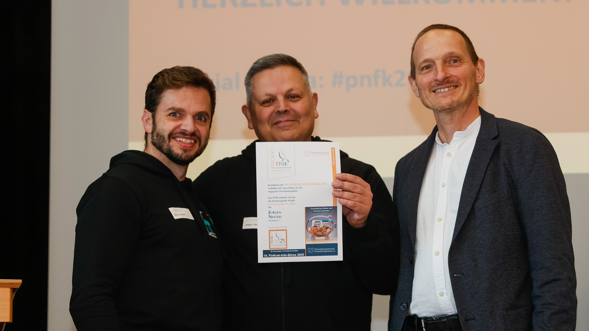 Von links: Der FinChamp Vorstand – vertreten durch Nico Litschke und Jürgen Neitzel – freuen sich über den Finken-Preis, verliehen durch Niko Mantseris, Vorstandsvorsitzender des Präventionsnetzwerks für Finanzkompetenz